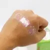 יד עם תחבושת דביקה שקופה הכוללת חזירים מצוירים ורודים וכוכבים על פרקי האצבעות. גוון העור בהיר, והרקע כולל רמז לחפץ ירוק.