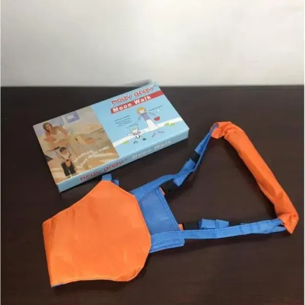 רתמת הליכה לפעוט, שכותרתה "הליכת ירח", מונחת על משטח כהה. הרתמה בצבע כחול וכתום ולצידה הקופסה שלה, עם איור ותמונות של ילד המשתמש ברתמה.