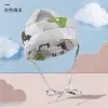 קסדת תינוק אפורה מרופדת עם עיצובים של בעלי חיים ירוקים ולבנים מוצגת על רקע שמיים כחולים ועננים מסוגננים. הקסדה כוללת שני קשרים ארוכים באזור הסנטר.