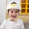 ילד חייכן עונד סרט מגן עם עיצוב שמש, עומד בתוך הבית. הילד לבוש בחולצה לבנה ונראה מאושר. ברקע ארון עץ עם מדפים צהובים.